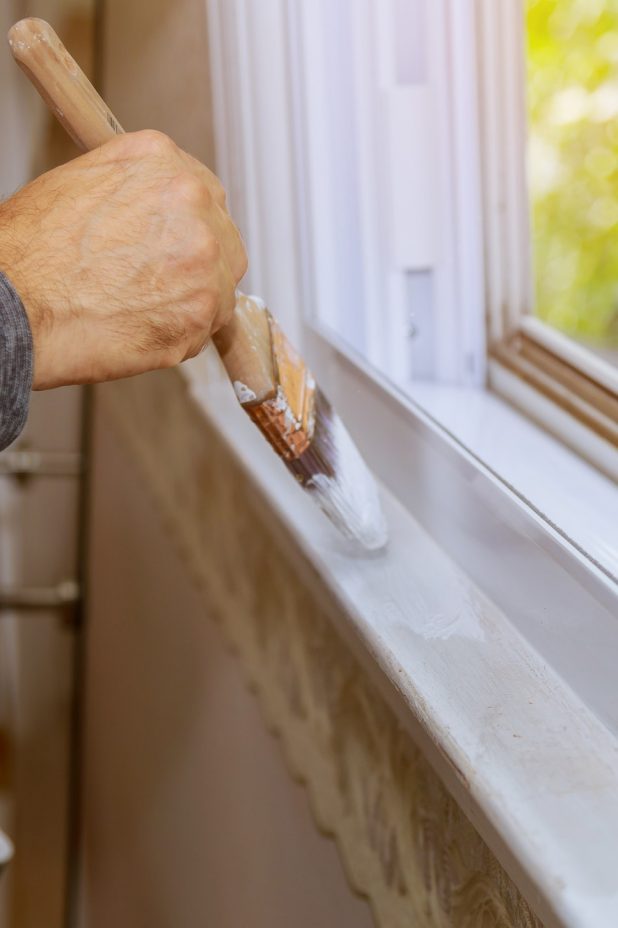 Worker painting window frame with white color at home